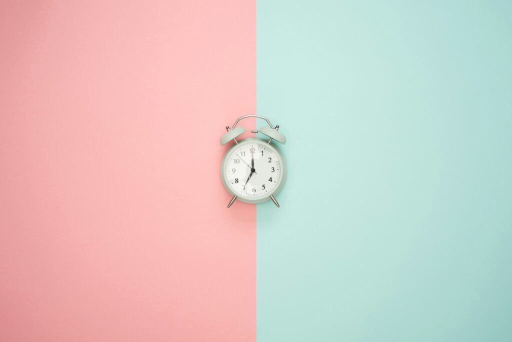 Silver alarm clock against a pink and pale green background
